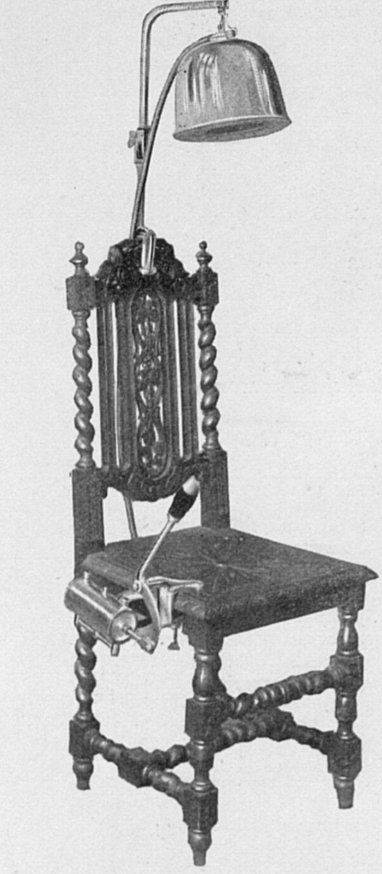 A black and white photograph of an upright Edwardian dining chair. It has an ornate design. Attached to the back of the chair is a metal cap, reminiscent of the drying machines in old-fashioned hair salons. Attached to the right-hand side of the seat is a pump which can be operated by hand.