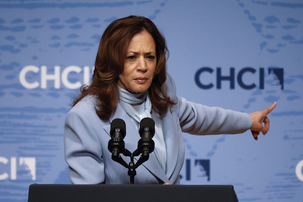 Kamala Harris stands at a lectern wearing a blue suit in front of a blue background.