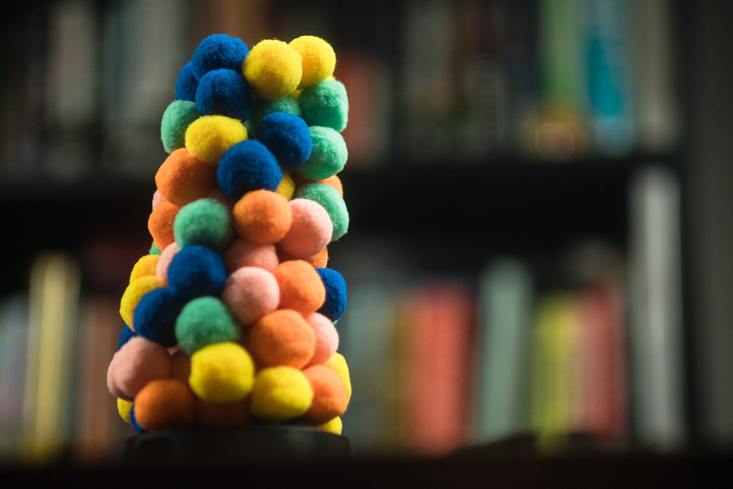 A tower of fuzz balls that comprise The Fuzzies with a bookshelf out of focus behind. The tower is leaning slightly.