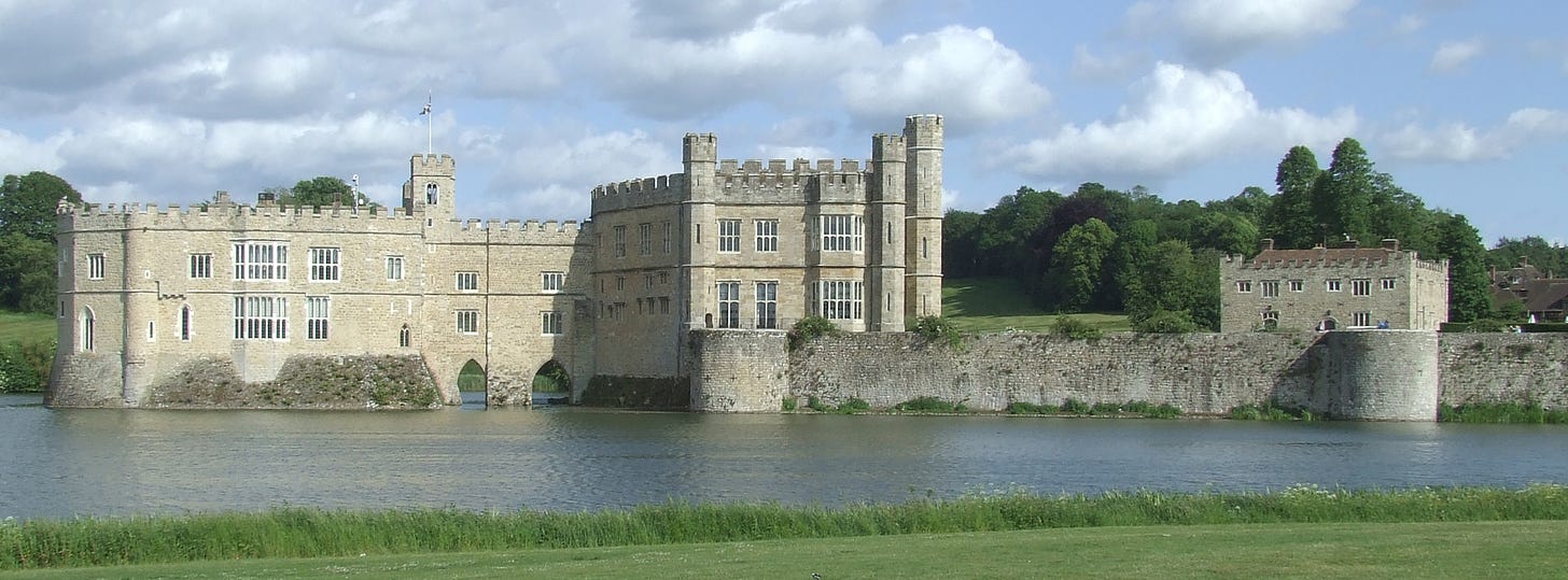 Part of Leeds Castle seen from across its surrounding lake, including the Keep/Gloriette, bridge, the New Castle in the bailey, and the Maiden’s Tower, halfway across the bailey.]