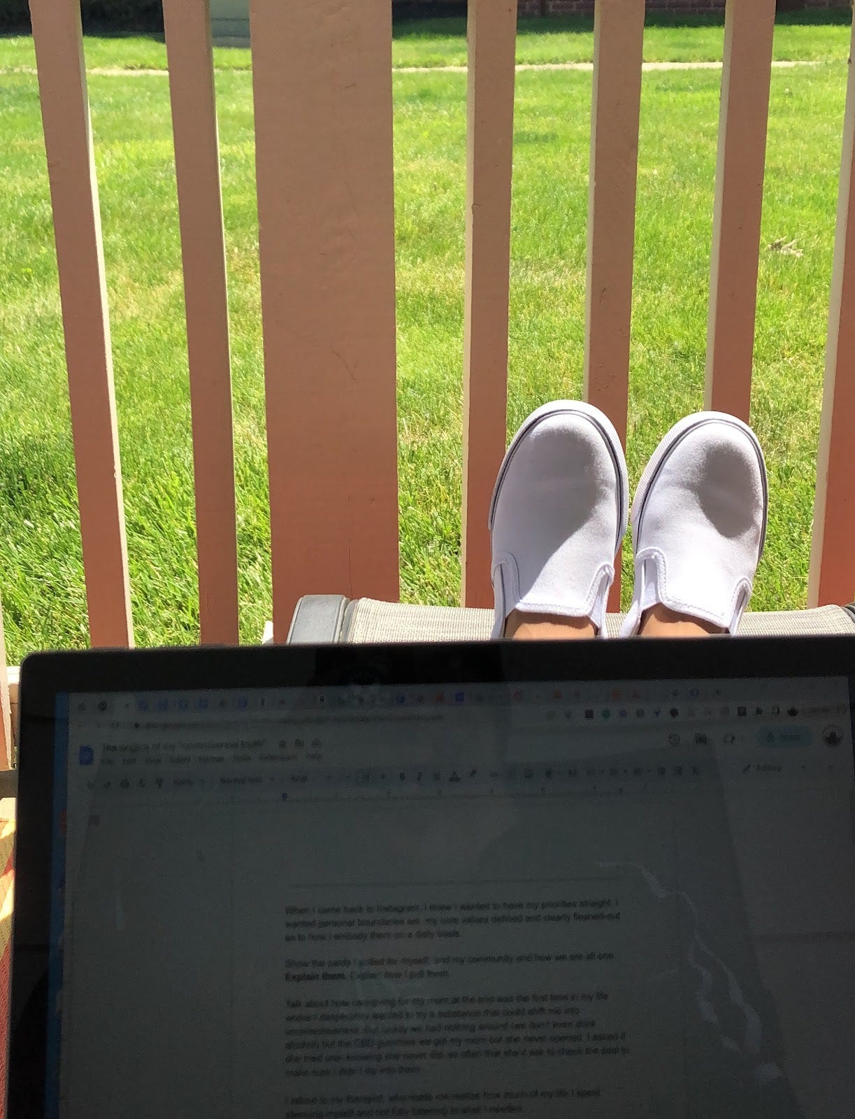 Photo of a first person point of view looking at a laptop with Google Doc up and feet perched on a stool outside on a sunny day on a porch.
