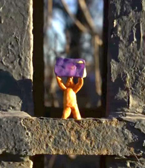 A yellow clay figurine raises a blank purple poster.
