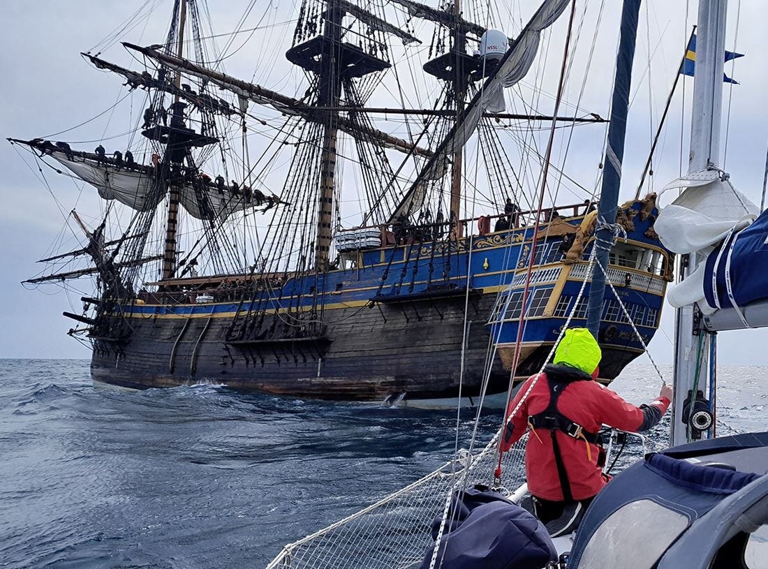 A replica of an 18th Century three-masted East India Company sailing ship with sailes furled takes a modern yacht in tow.