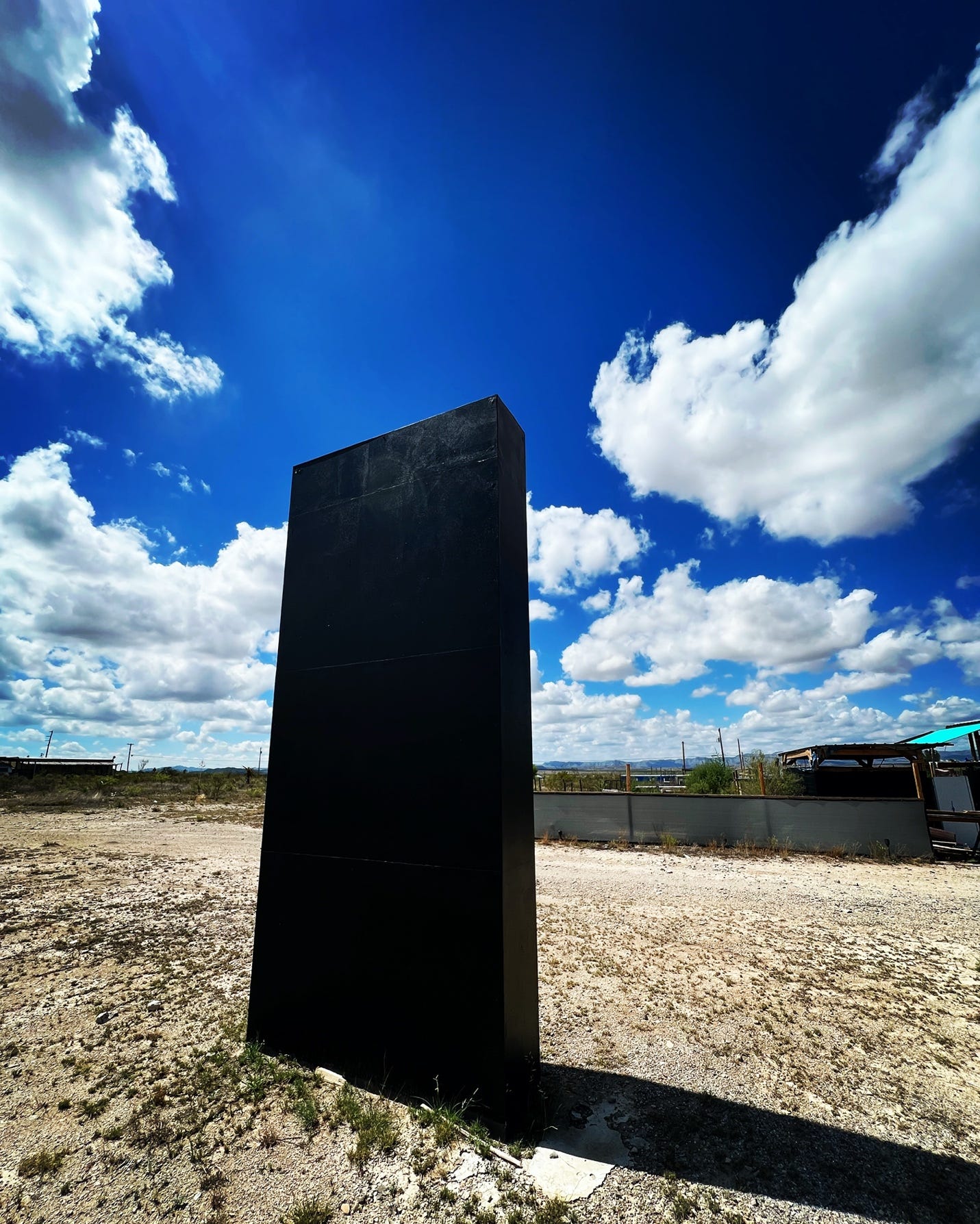 A tall black rectangular object in a dirt field

Description automatically generated