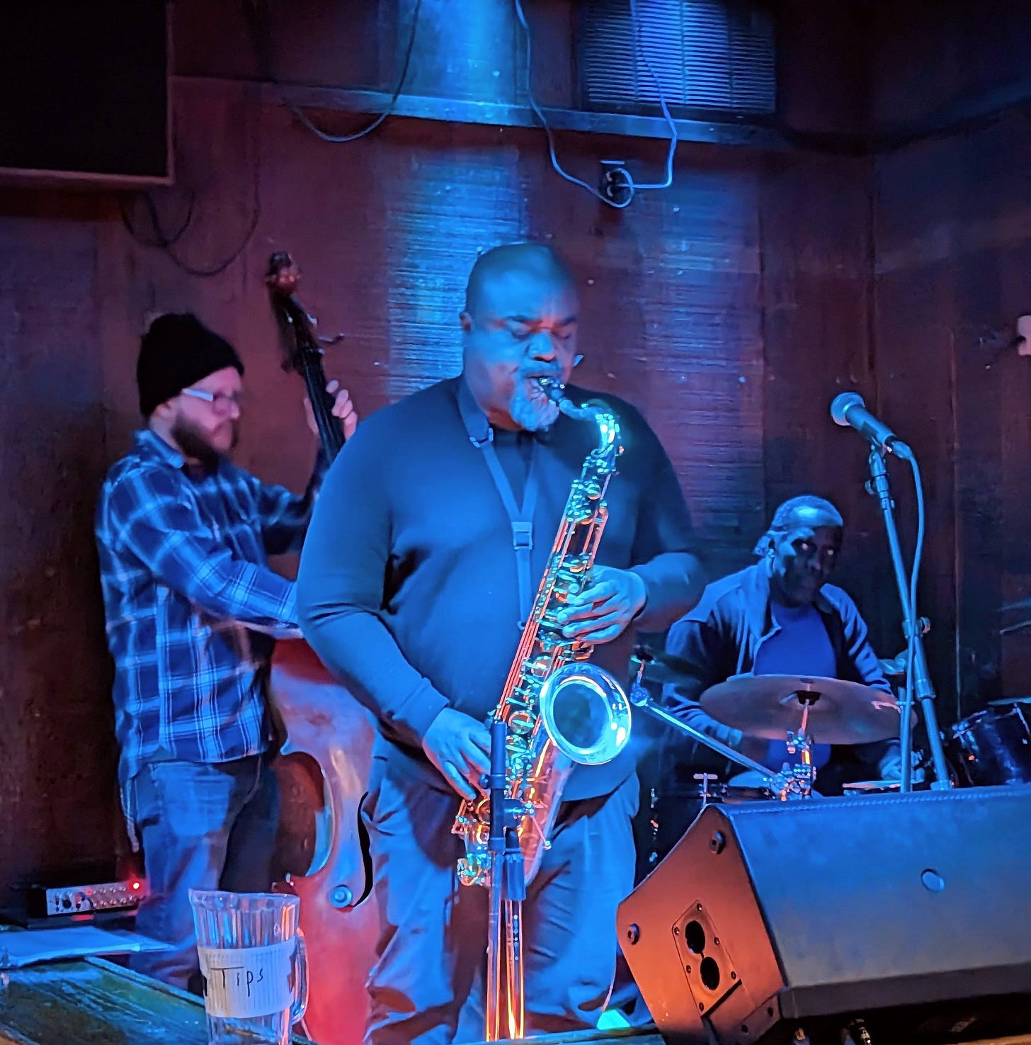 Saxophonist in the foreground, flanked by upright bassist and drummer