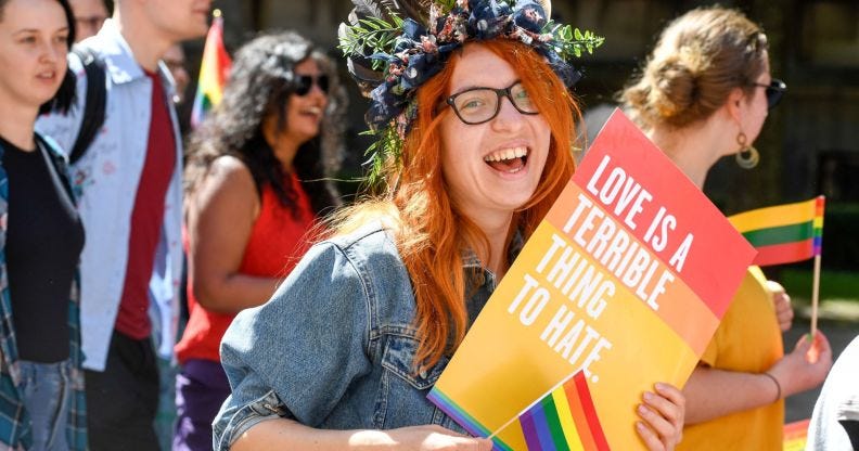 An LGBTQ+ activist holds a sign saying 'love is a terrible thing to hate'