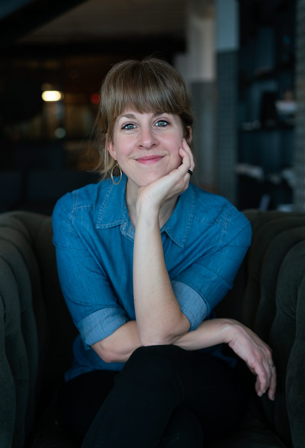 Jewish food writer Leah Koenig author photo, a Caucasian woman seated looking directly at the camera with her hand on her chin.