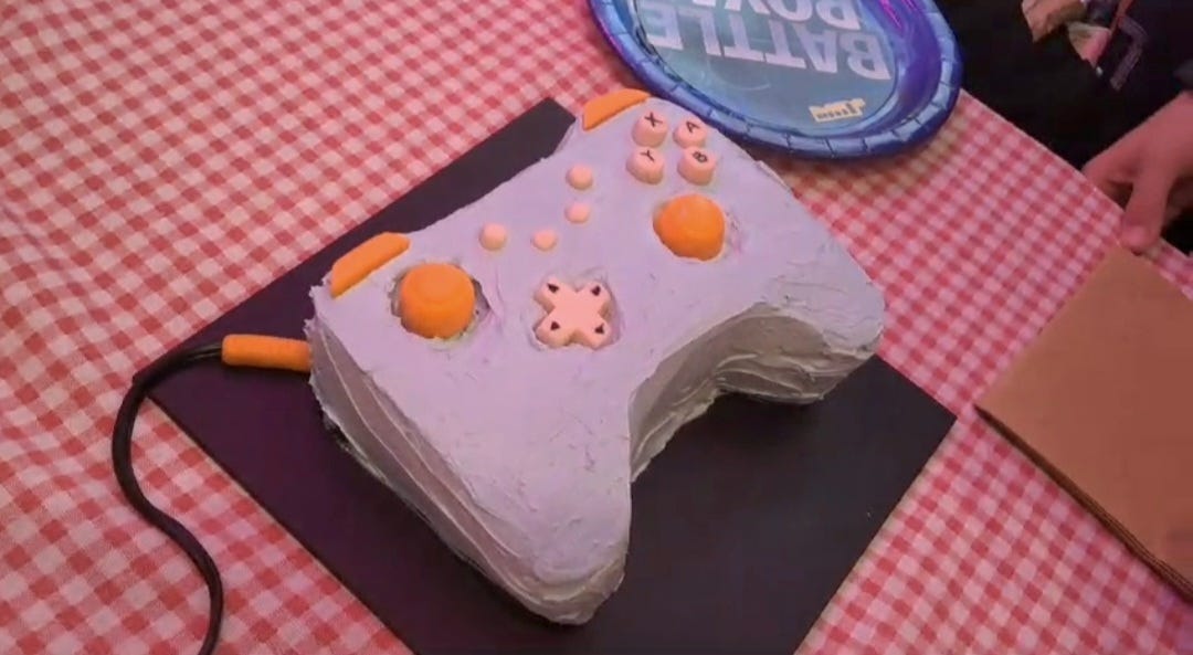 A cake that looks like a game controller sitting atop a black cakeboard on a red and white check tablecloth