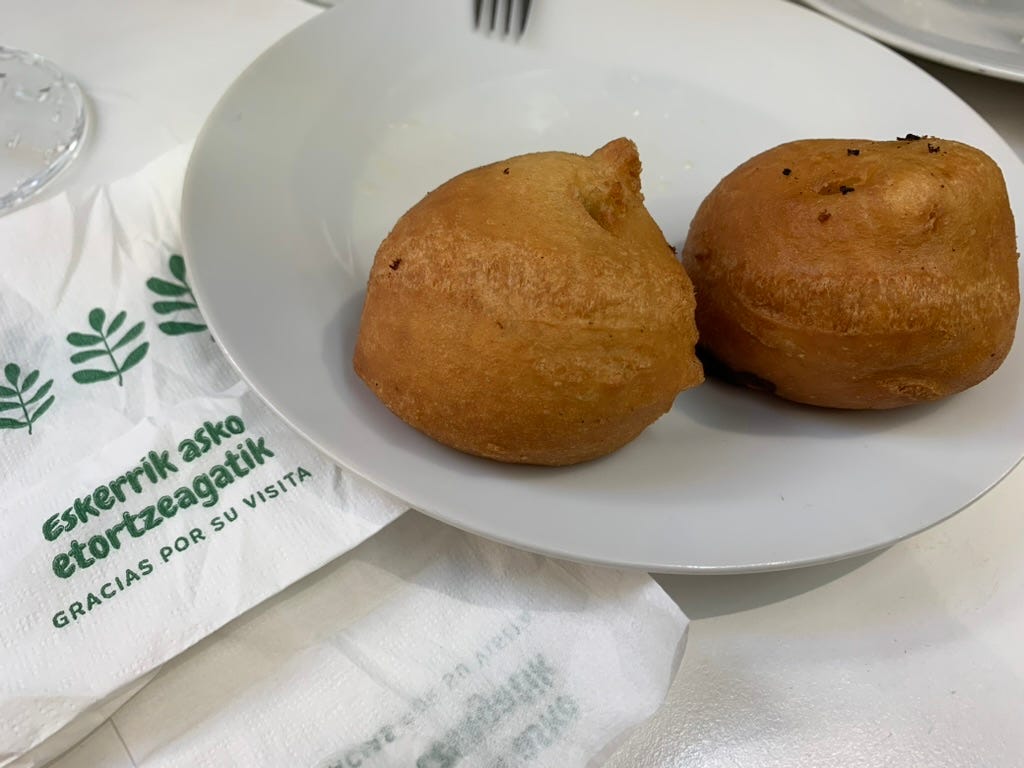 Two rather boring looking fried balls sit next to a napkin that says Thank you for your visit in Euskera and Spanish.