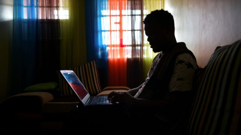 A photo of a man working on his computer in a dark room.