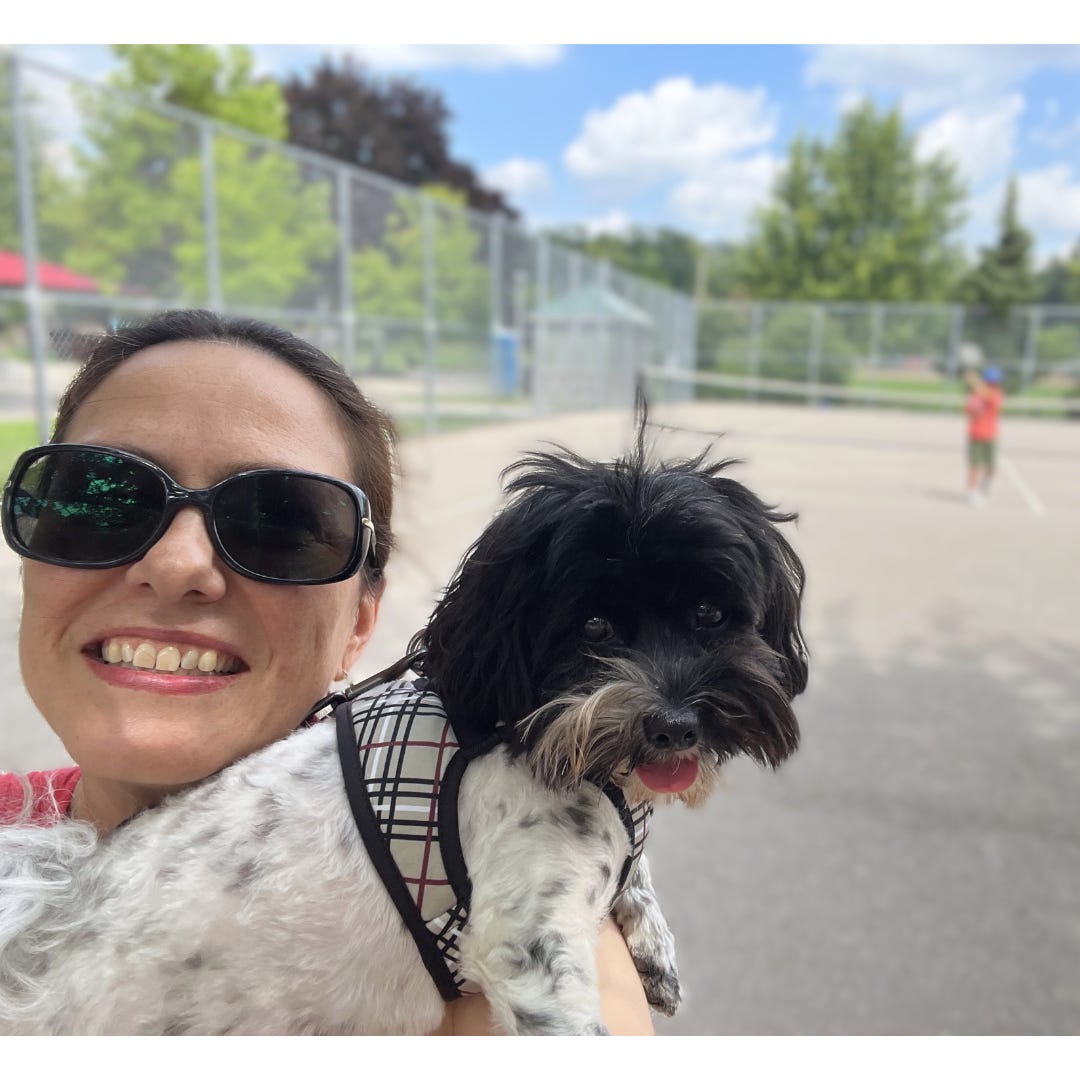 Freelancer Lisa Orchard smiling while holding her small black and white dog on a tennis court