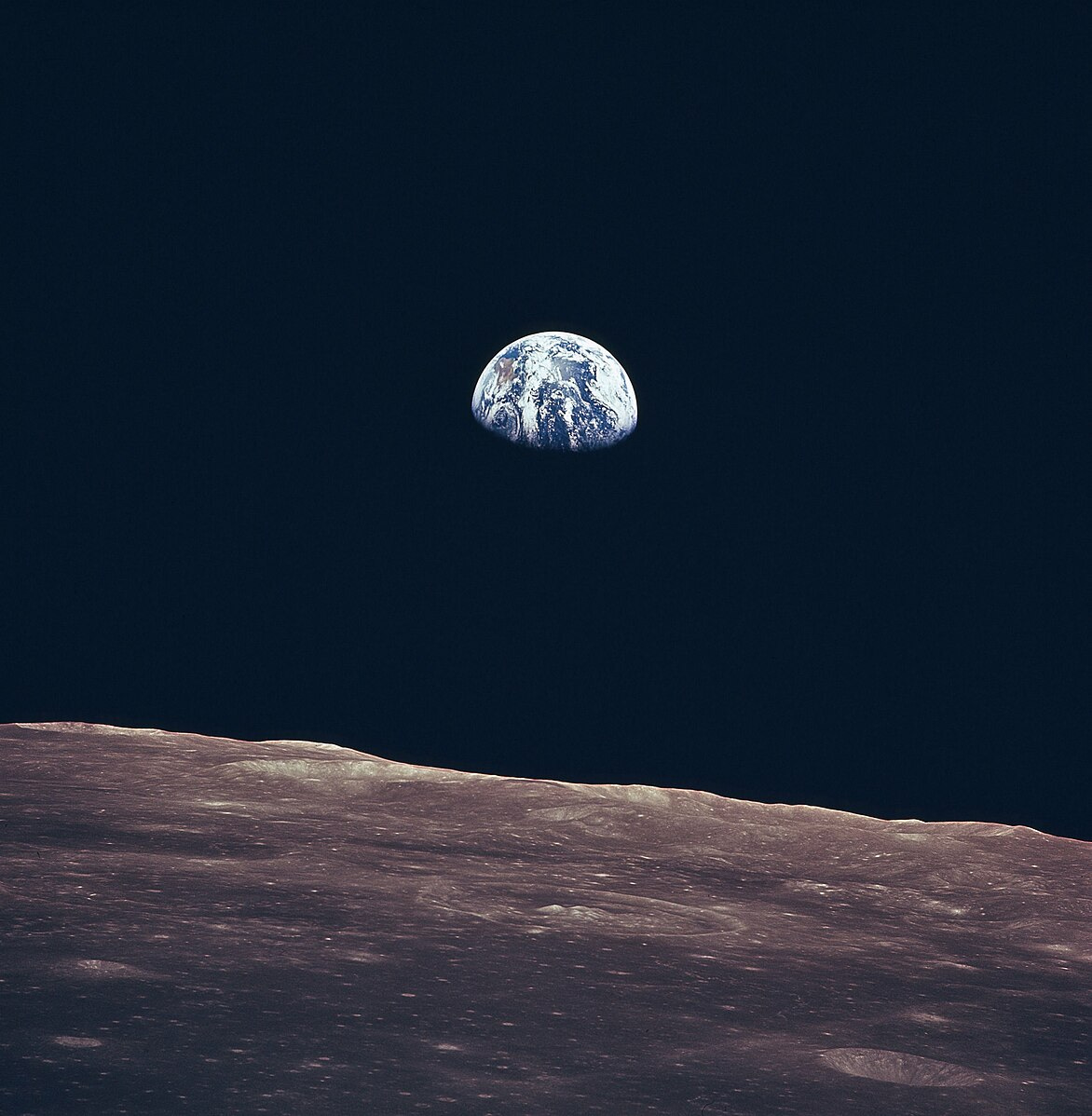A color photo of the cratered surface of the Moon against a black starless sky. A half-shadowed distant Earth hangs in the sky.