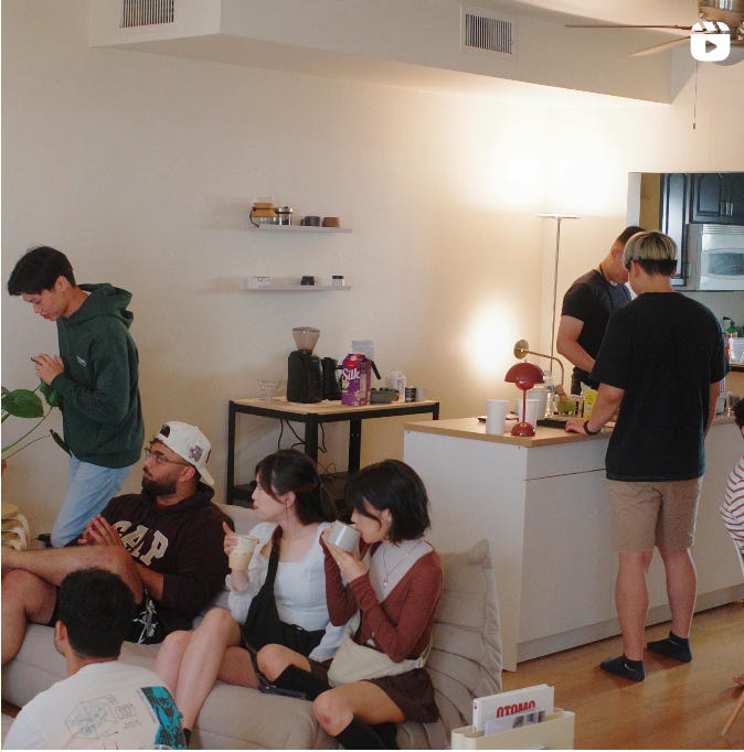 A room full of people enjoying coffees. Some are sitting on a beige couch while the host makes coffee for their friends in their at-home coffee bar