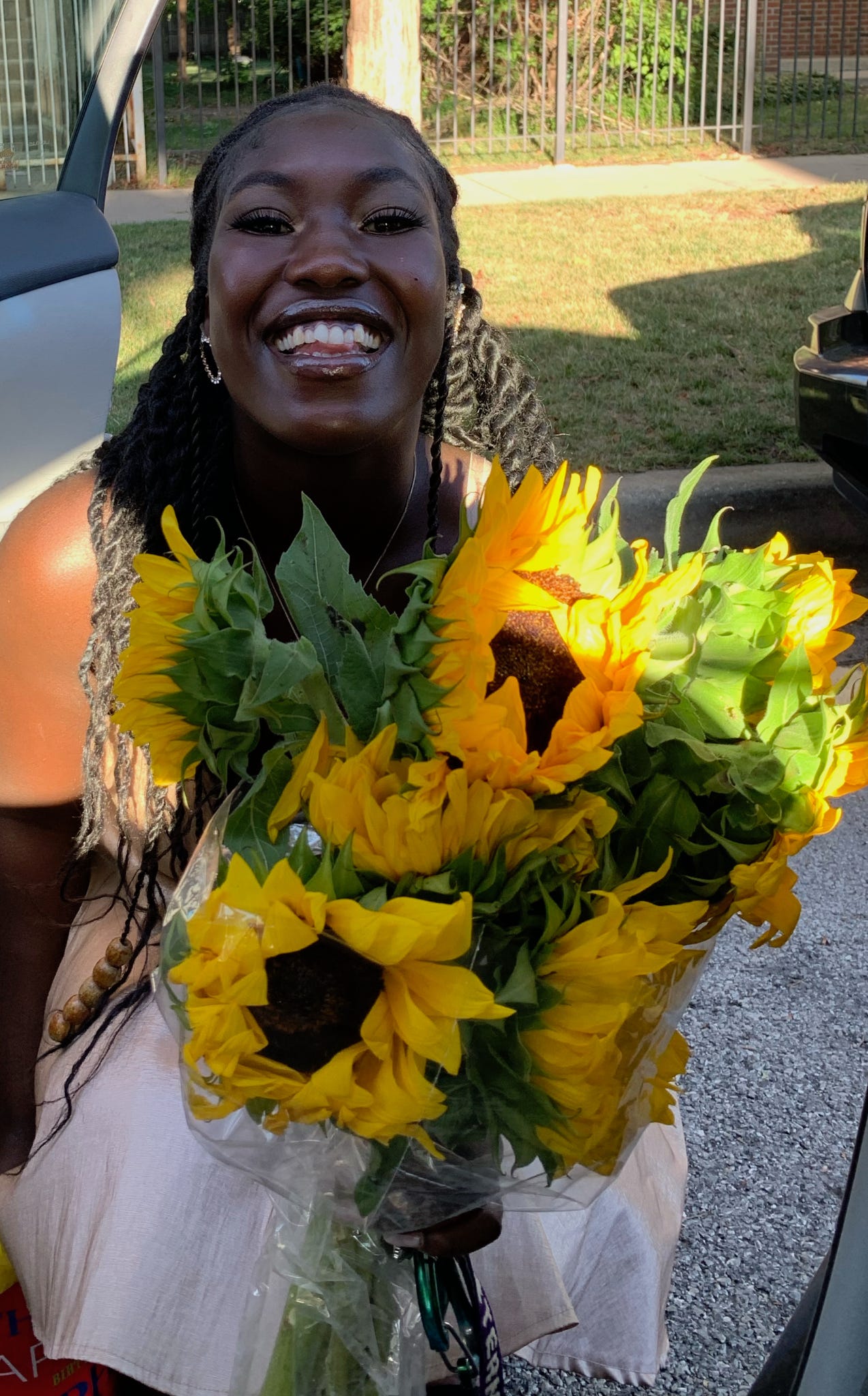 ismatu smiles with a bouquet of sunflowers in a golden dress.