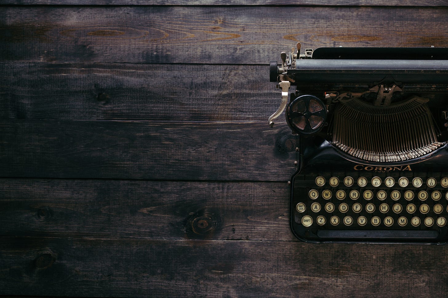 A black Corona typewriter sits on a brown wooden desk.