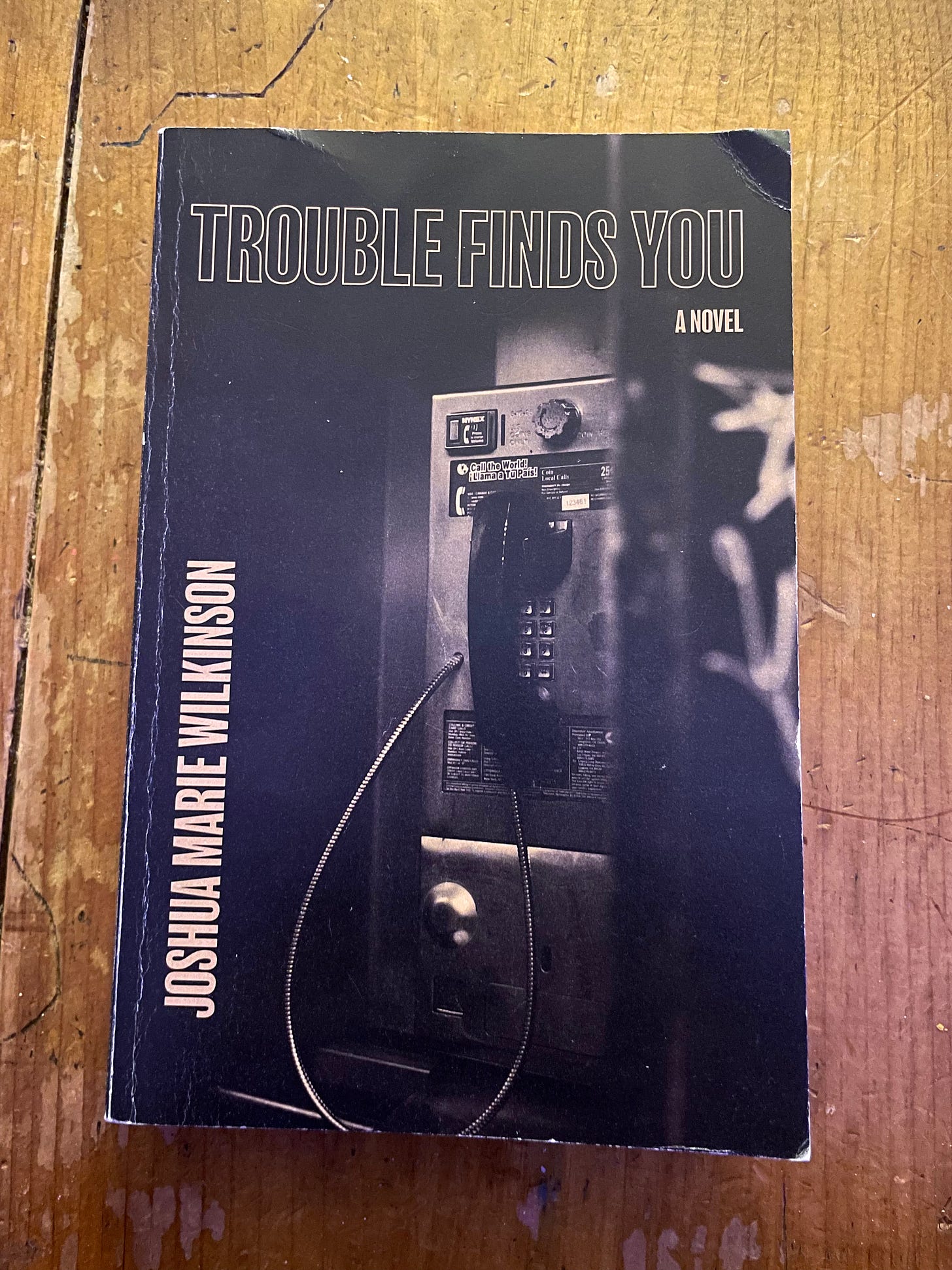 book on a wooden coffee table: 'Trouble Finds You' by Joshua Marie Wilkinson