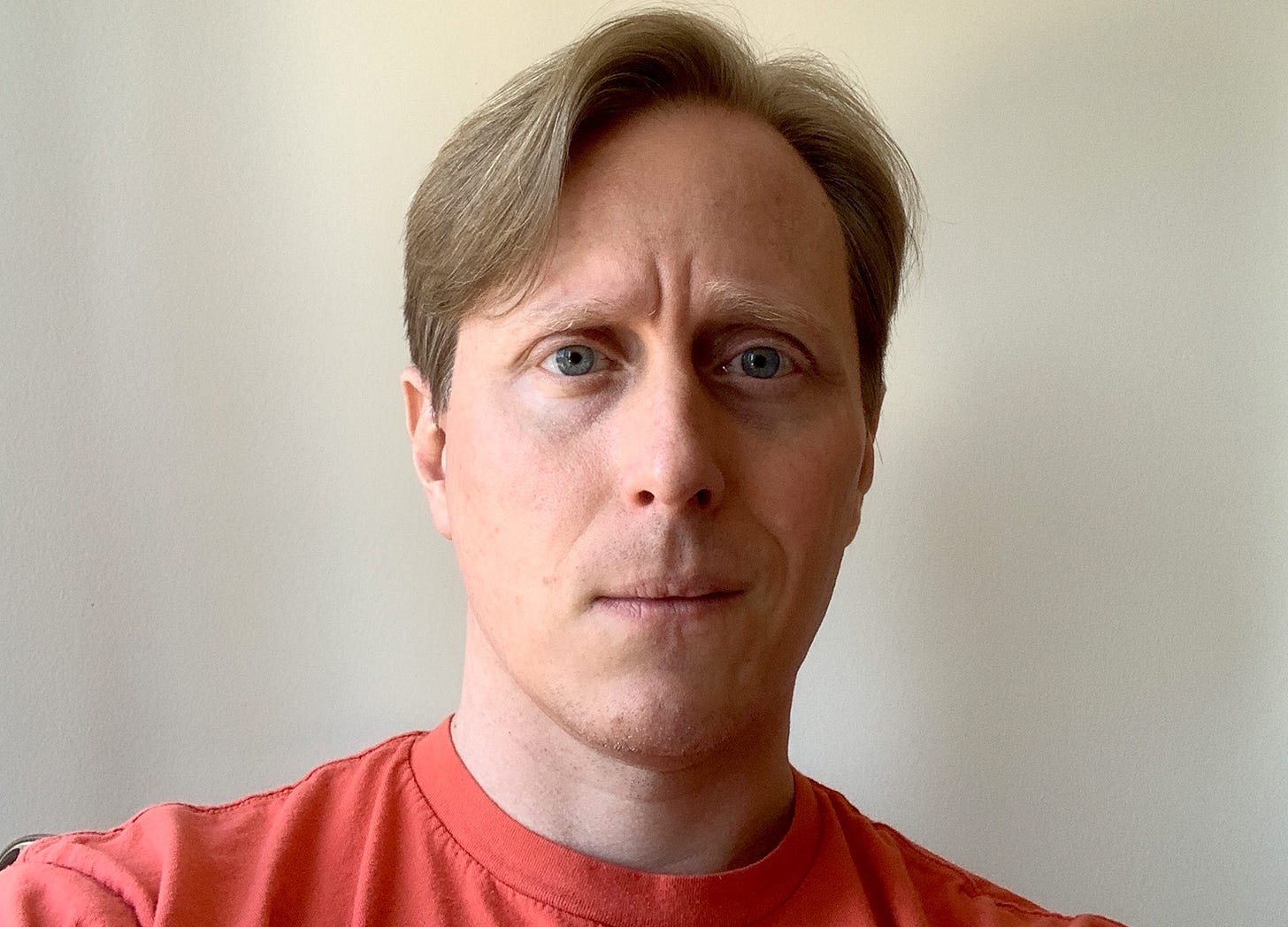 A headshot of journalist Tom Scocca wearing an orange t-shirt