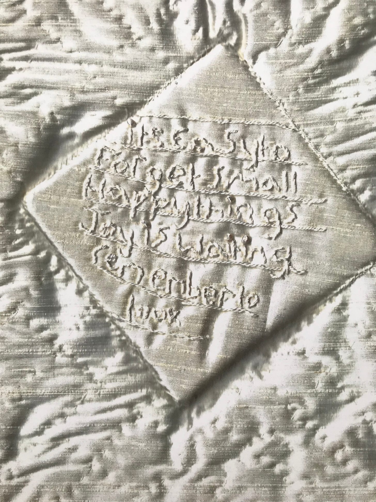 Book of Hours cover, image of quilted satin fabric with stitching in a diamond shape at the centre with the text "It’s easy to forget small happy things joy is waiting remember to look."  in hand stitch.