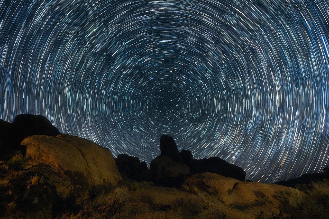 Stars cast a bright series of circles over brown-black mountain and stone formations. 