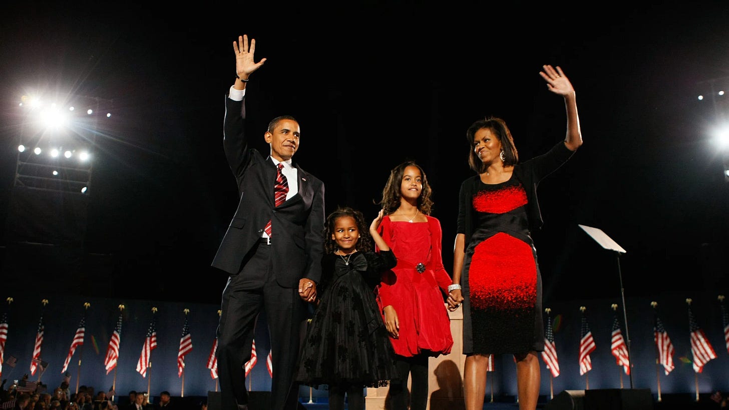 This photo, taken by Joe Raedle of Getty Images, shows, from left to right, President-Elect Barack Obama, his daughter Sasha, his daughter Malia, and his wife Michelle, standing on stage in Chicago's Grant Park on the night of 4 November 2008. Several American flags surround the family. Both Barack and Michelle Obama wave to the assembled crowd, Barack with his right hand and Michelle with her left hand. This photo, taken by Joe Raedle of Getty Images, shows, from left to right, President-Elect Barack Obama, his daughter Sasha, his daughter Malia, and his wife Michelle, standing on stage in Chicago's Grant Park on the night of 4 November 2008. Several American flags surround the family. Both Barack and Michelle Obama wave to the assembled crowd, Barack with his right hand and Michelle with her left hand.