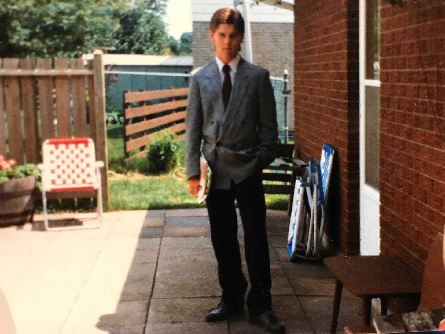 A grainy picture of myself wearing a jacket and tie in my parents' backyard.