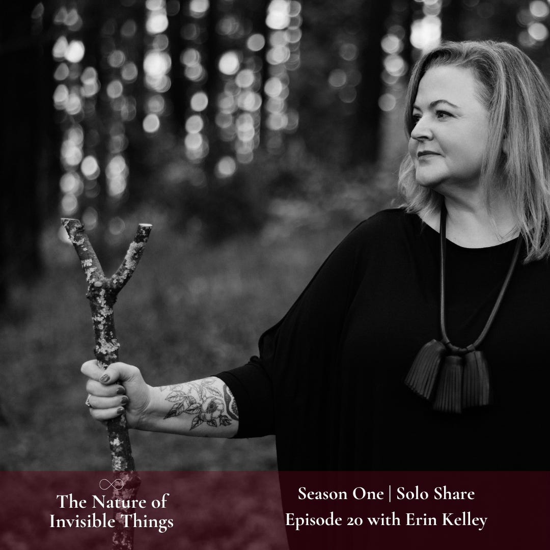 A black and white photo of Erin standing in the woods holding her stang. She is wearing a black tunic and leather necklace. Her fingernails are painted and we can view some of her floral tattoos. Erin is not looking at the camera, but over her shoulder.