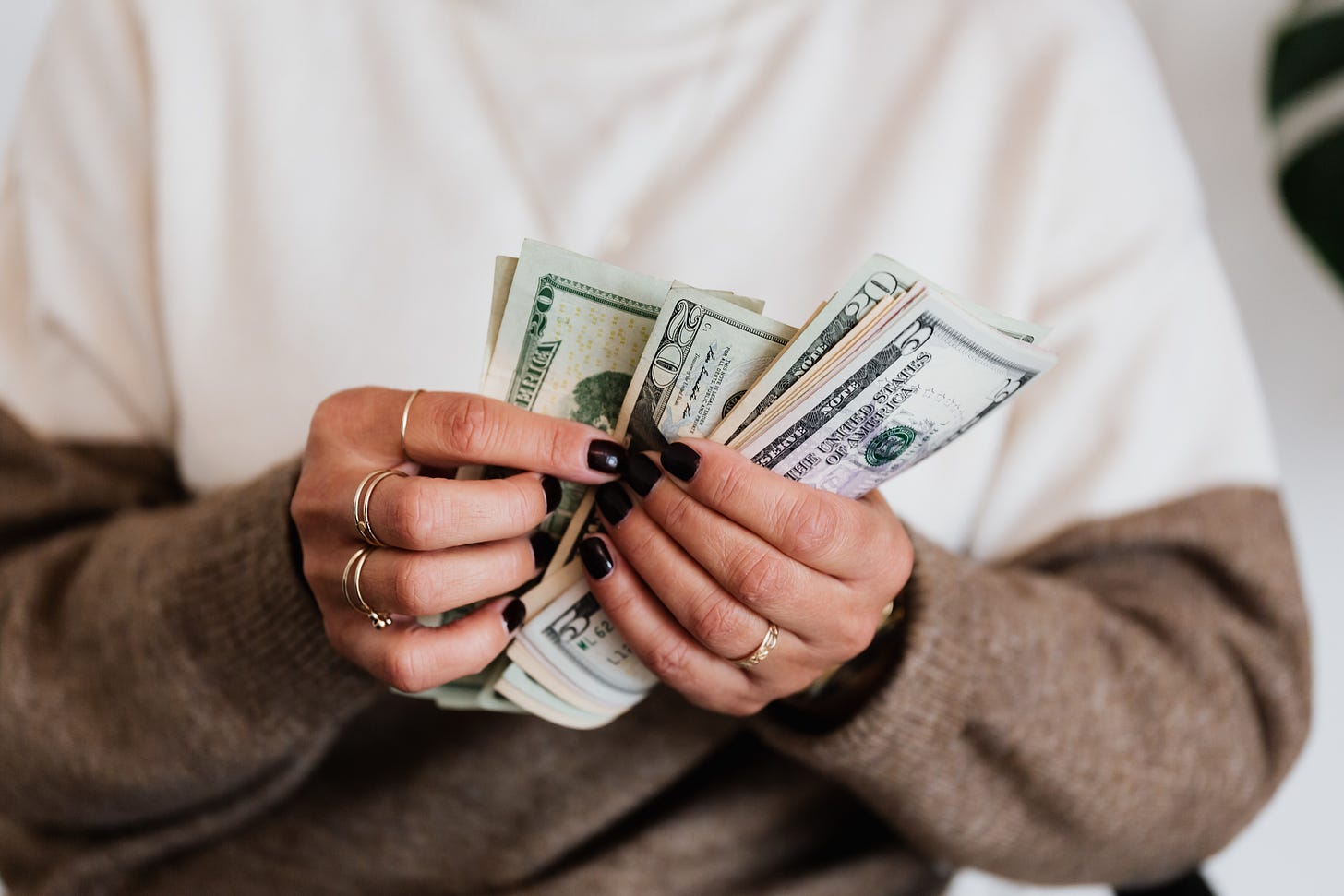 mulher segurando várias notas de dollar com as unhas pintadas de preto com aneis dourados