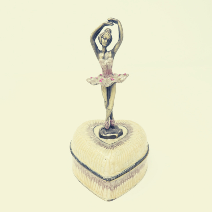 Photo of a small music box with a ballerina on top. Pink hues.