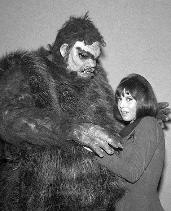 This may contain: a woman standing next to a man dressed as a gorilla in a black and white photo