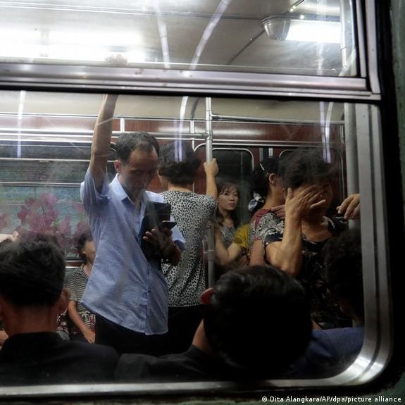 Subway passengers sit or stand behind a windowpane of an underground carriage in Pyongyang, North Korea. 