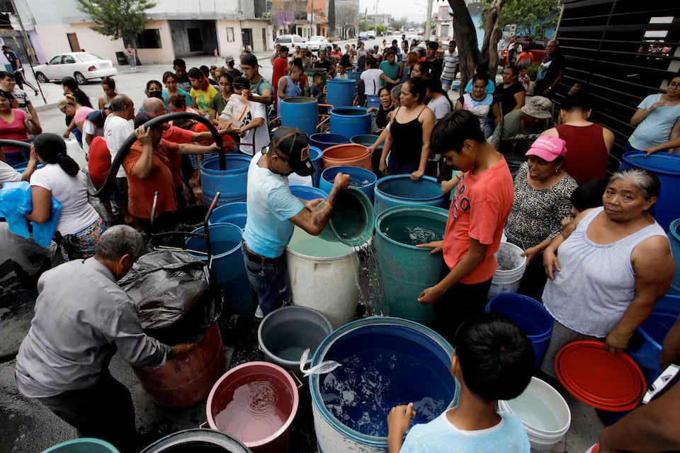 A crowd gathered around a life saving water truck getting containers filled from buckets to 30 gallon drums.