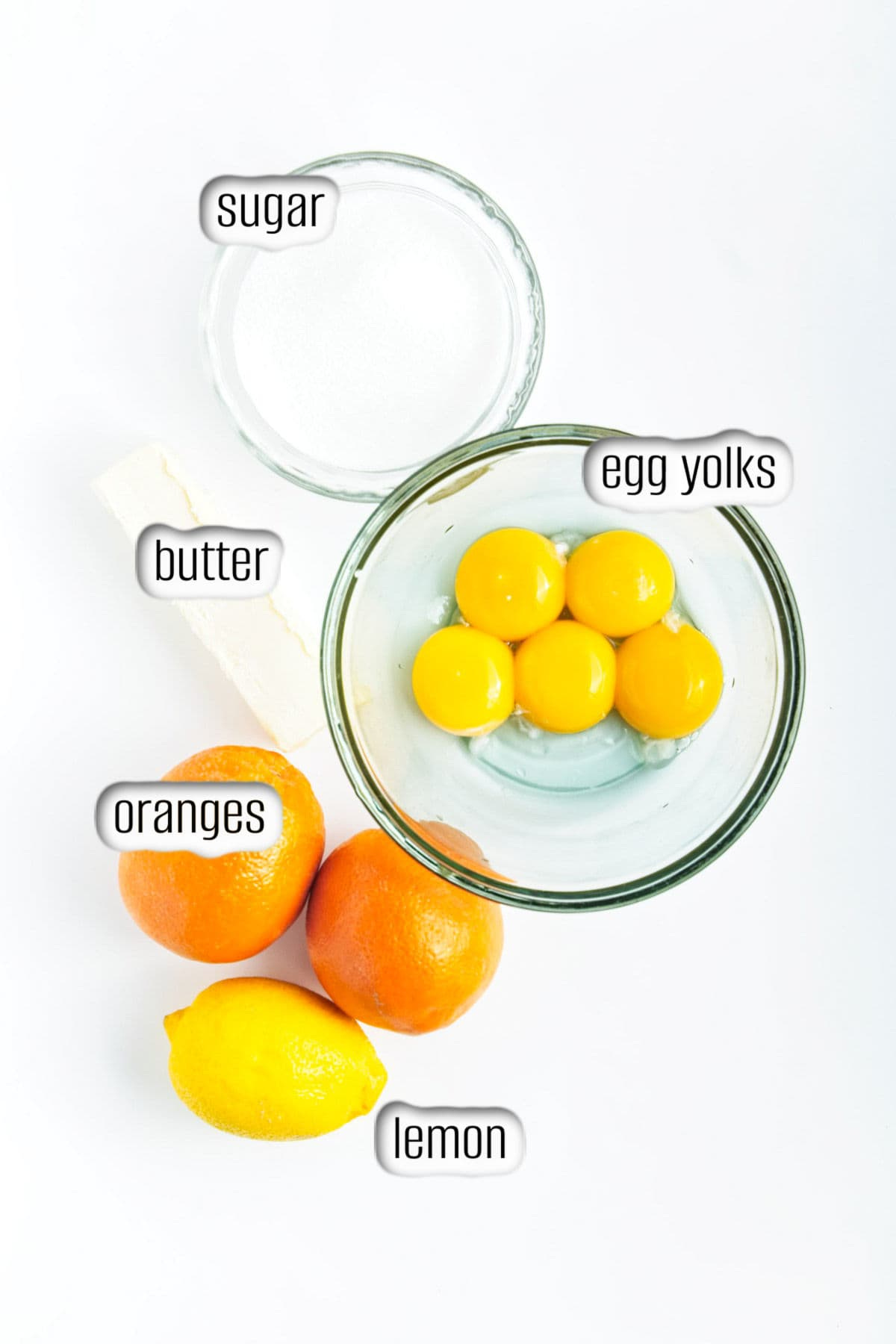 Lemon, oranges, butter, sugar and bowl of egg yolks.