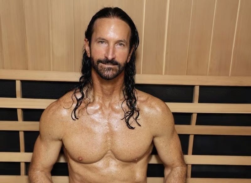 A muscular, lumpy man with a brown beard and long, curly brown hair. He's shirtless, of course, because you can't show you're anti-aging if your tits aren't out. He's smiling awkwardly at the camera. He's wet.