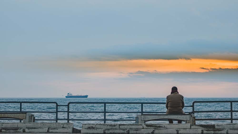 Man sitting alone on the pier watching a ship sale by.