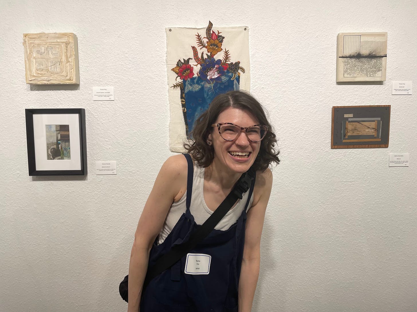 snapshot of a white woman smiling and laughing in front of 5 pieces of collage art of varying sizes