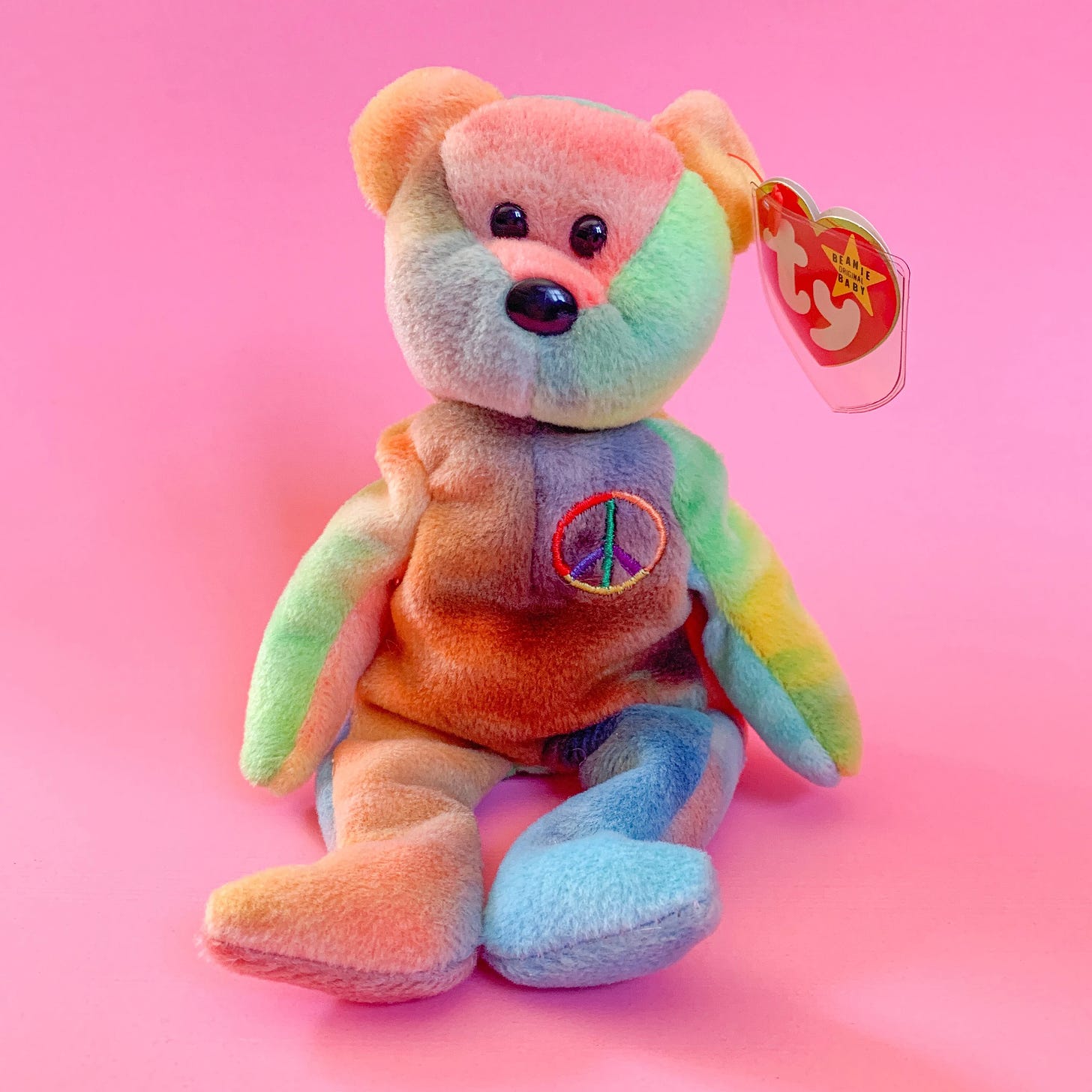 In image of a tie-dye Beanie Babie named "Peace" in front of a pastel pink background.