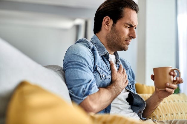 Young man feeling sick and holding his chest in pain while drinking tea in the living room