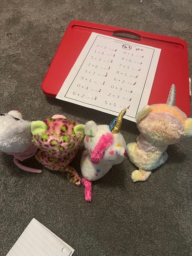 Small stuffed animals sitting in front of a math paper on a writing board on the floor