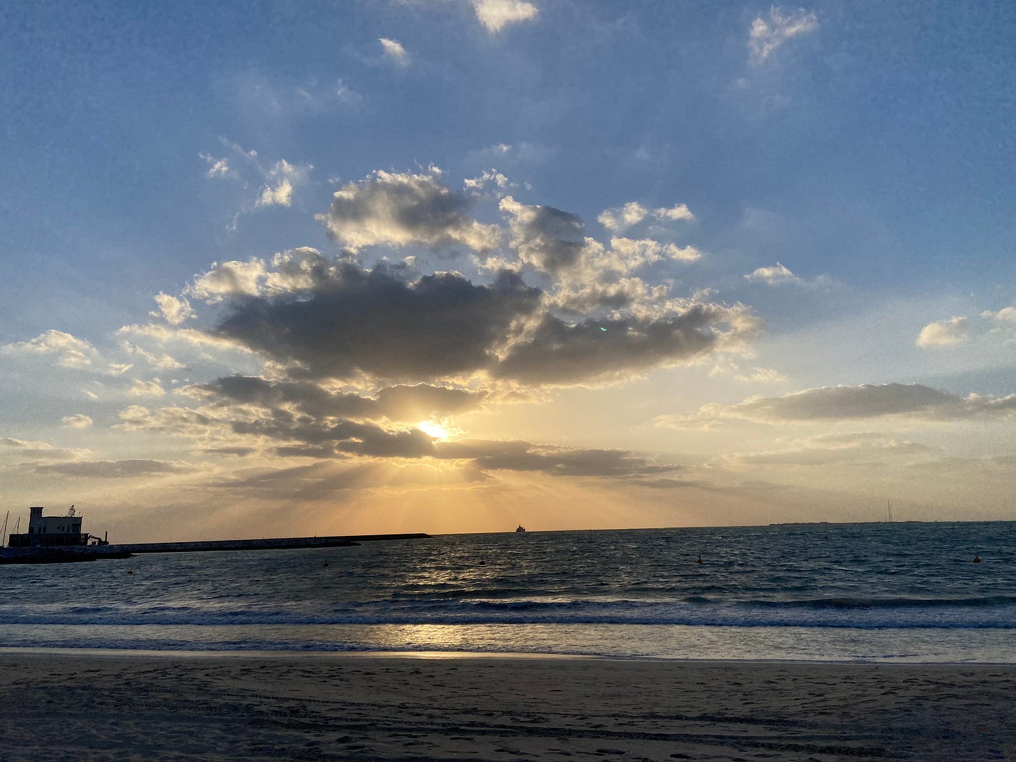 Photo of sunsetting with a few clouds at the beach. On the left-hand side there is a small Gulf Arabic looking watch tower