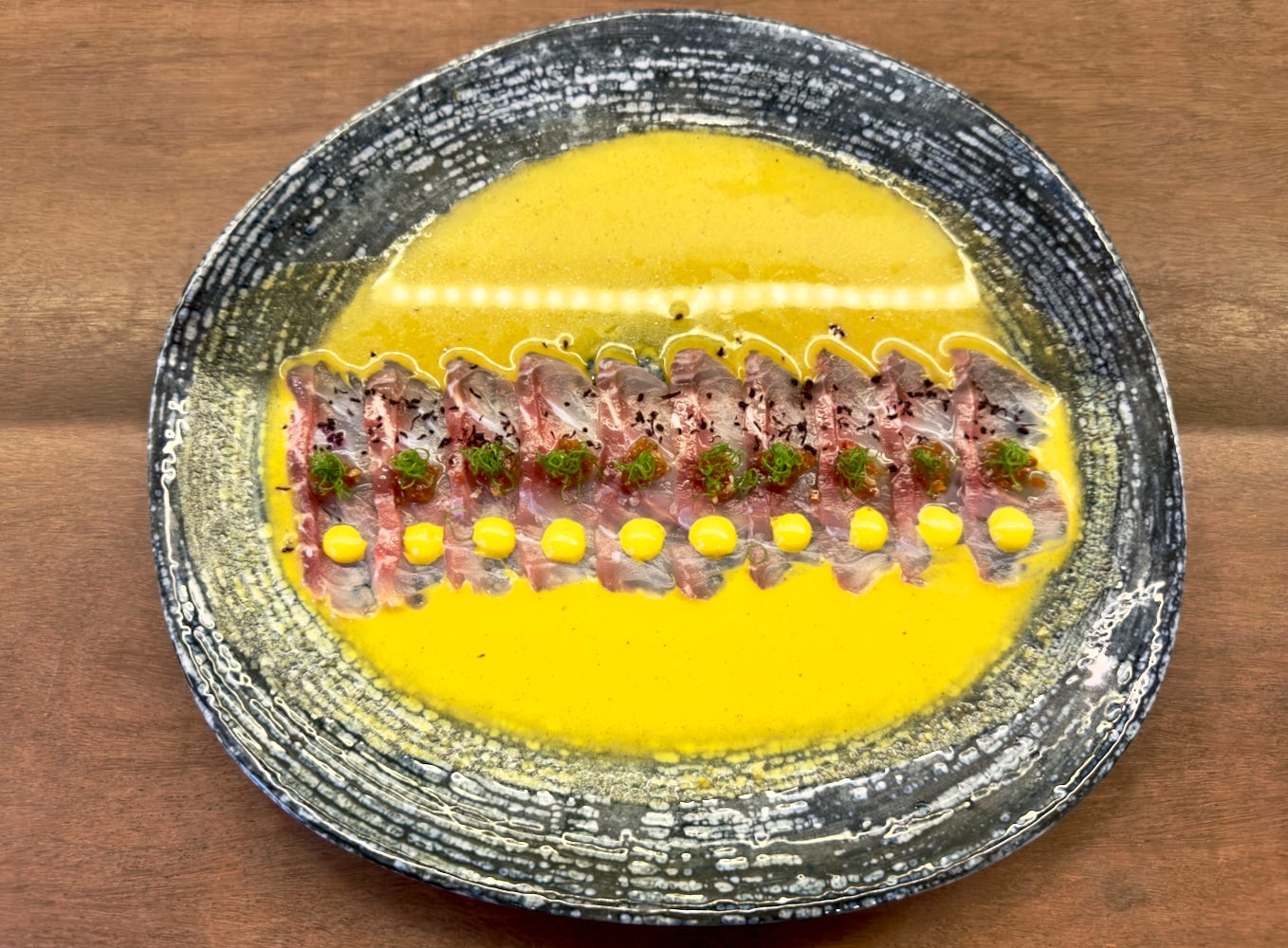 Beautiful plate of tiradito with perfectly sliced fish in a bright sea of Peruvian yellow pepper.