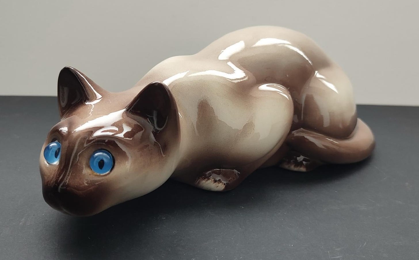 Porcelain crouching Siamese cat with blue eyes
