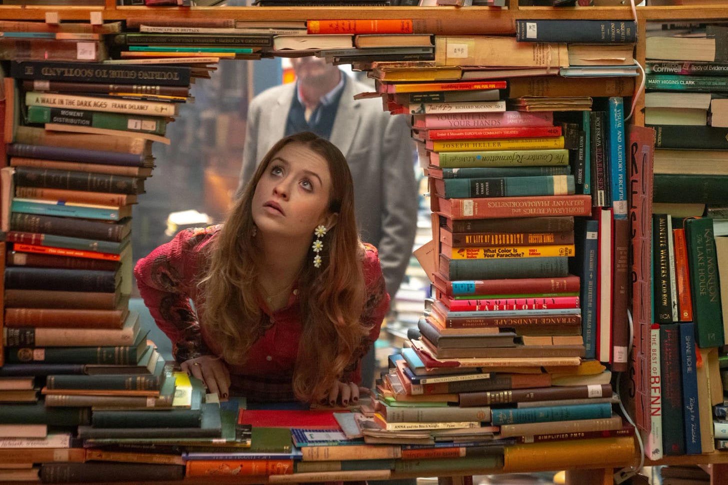 Photo de la série Extraordinary où l'héroïne, Jen, regarde à travers un trou, une arche, faite de livres.