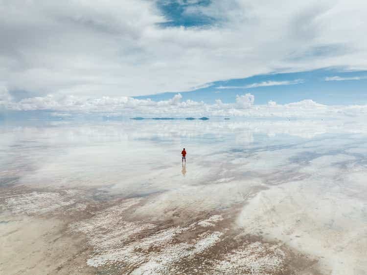 One man looking across a flooded salt pan during the day seen from a drone perspective, Salar de Uyuni, Bolivia