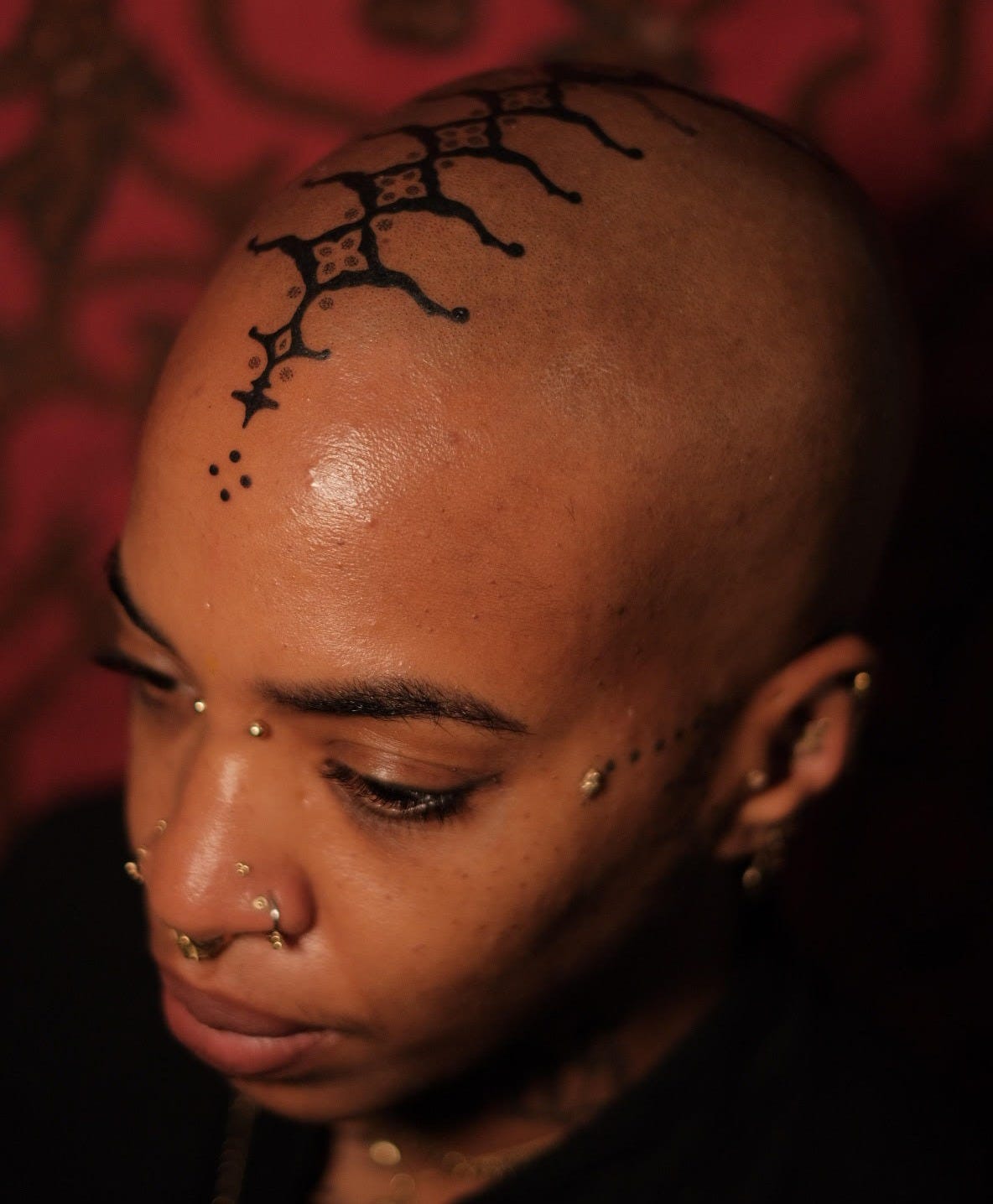 brown skin woman with a tribal tattoo descending from the middle of her forehead across her scalp to the back of her head