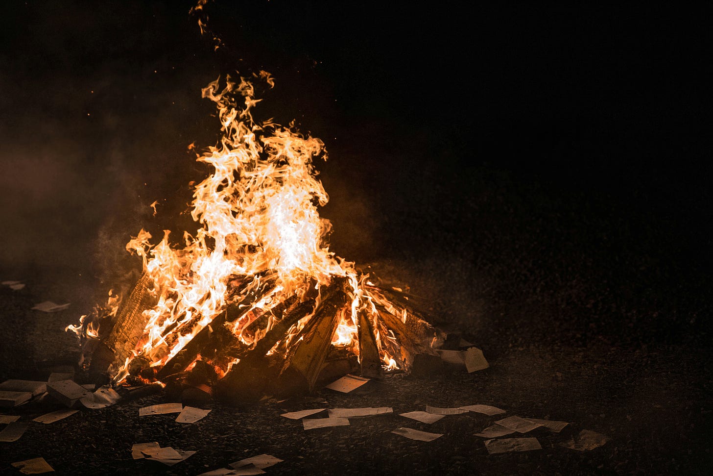 A roaring bonfire at night. In the foreground are scattered papers.