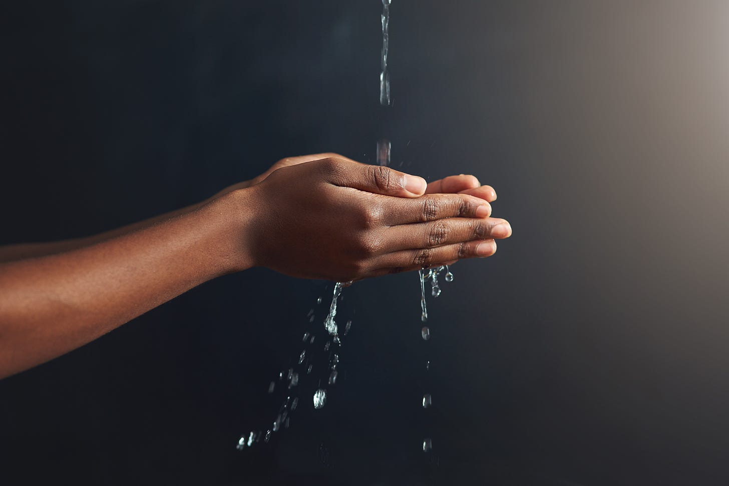 Two brown-skinned arms extended, palms upon to the sky, as water spills into the hands and between the fingers