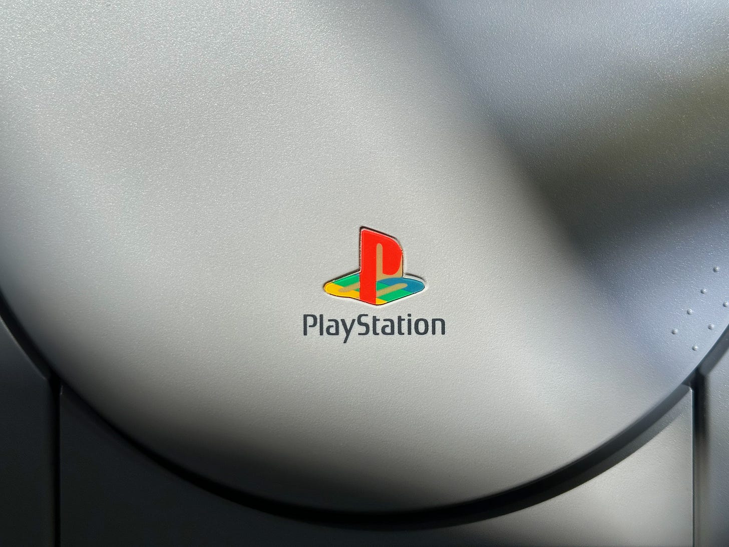 Closeup photograph of the PlayStation logo in red, yellow, green, and blue on the lid of a PS1.