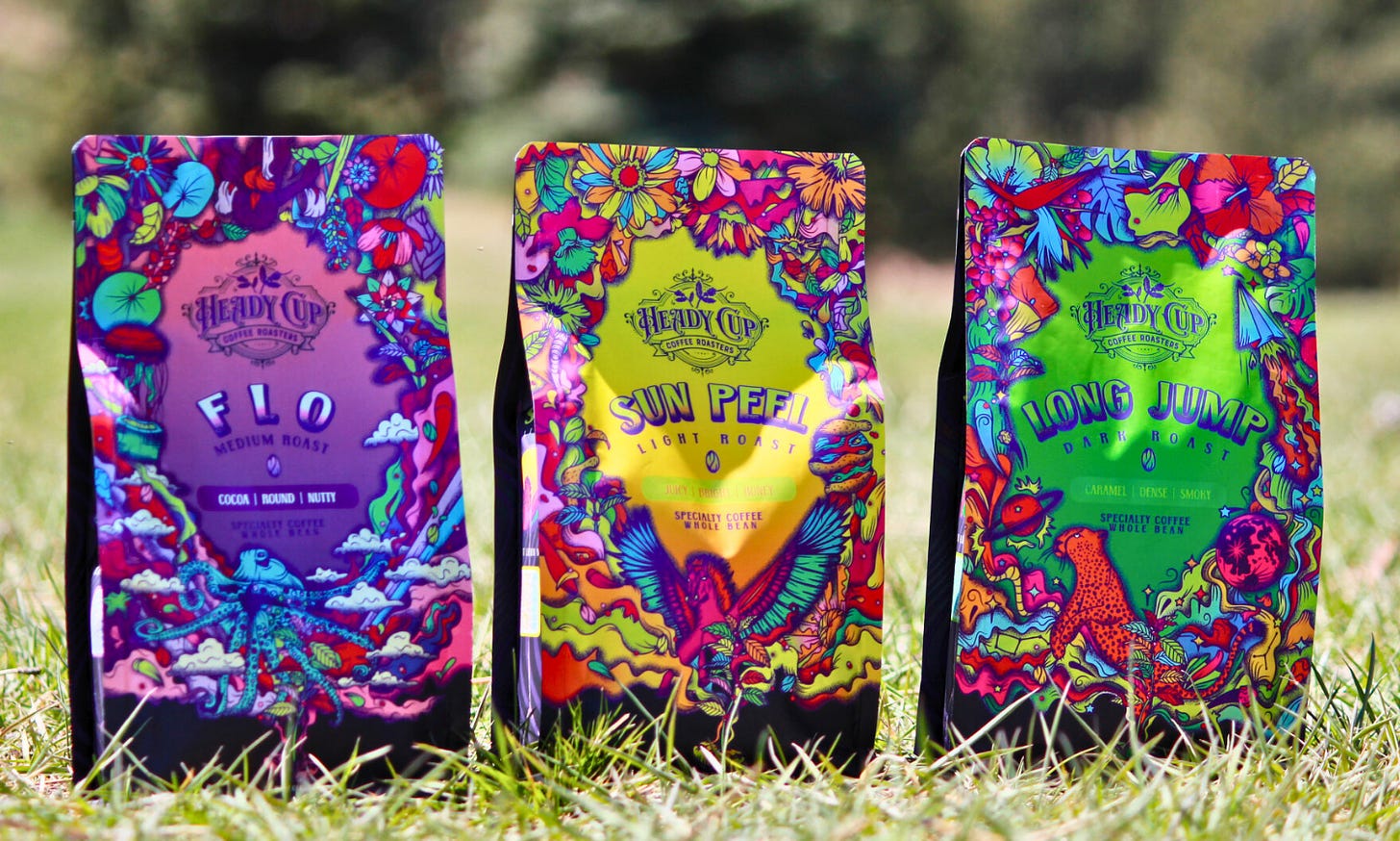 Three 1970s inspired colorful floral and animal print designs on coffee bags sitting in the grass.