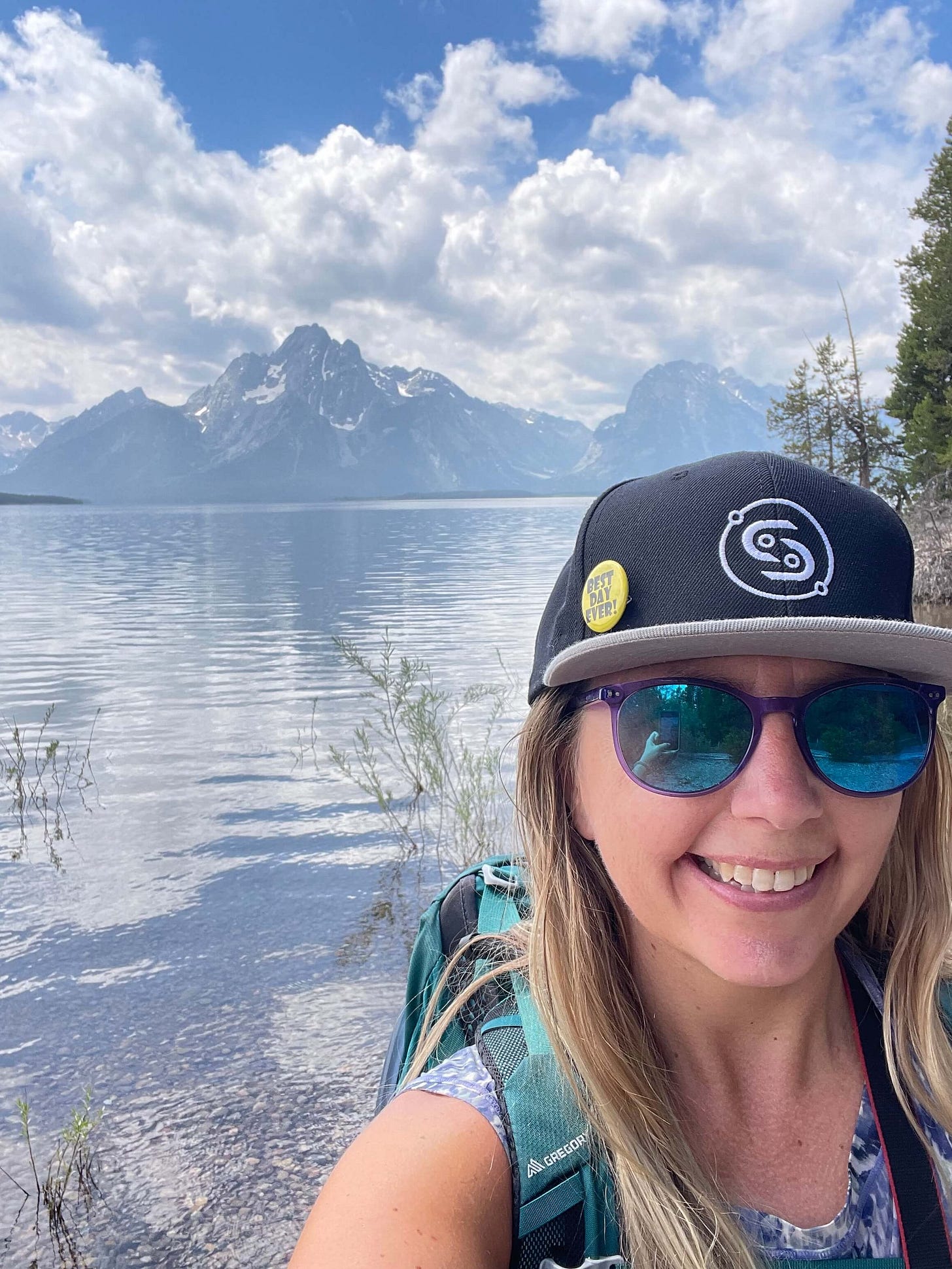 Selfie of Cassidy grinning with Grand Teton in the background and an expanse of lake in between.