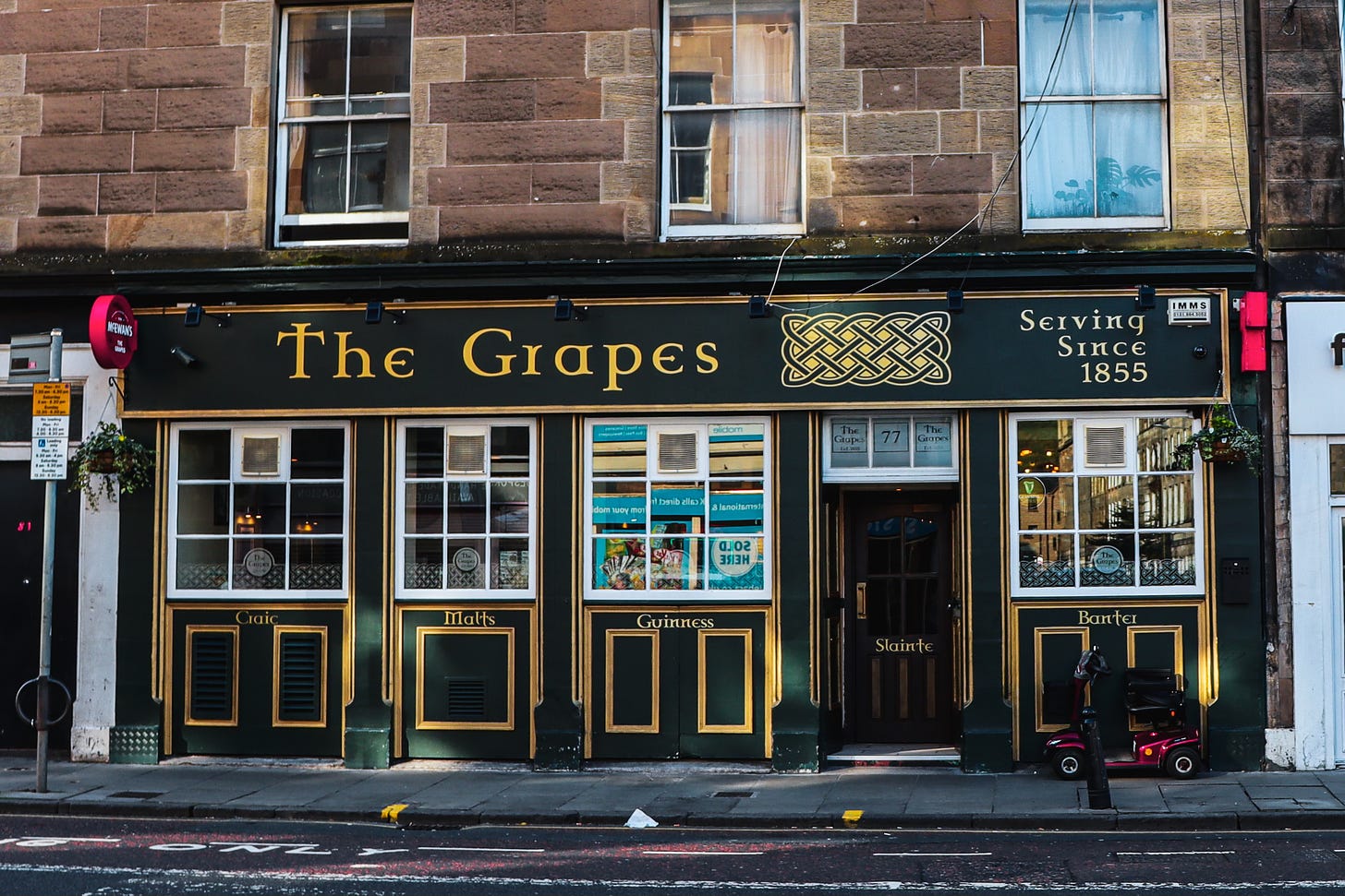 The Grapes pub photographed from across the street. Dark green sign with yellow writing.